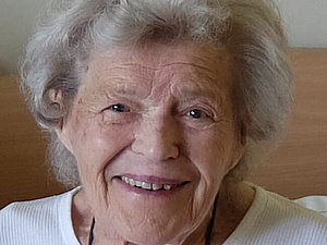 Eine ältere Dame mit weißer Dauerwelle lächelt freundlich in die Kamera