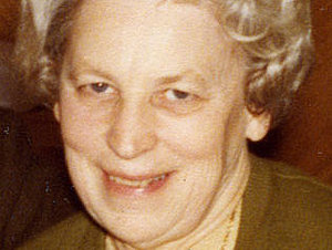 Eine ältere Dame mit weißer Dauerwelle lächelt verschmitzt 