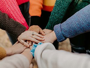 Gruppe Frauen, die im Kreis stehen und ihre Hände in der Mitte übereinandergelegt haben. 