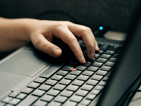 Eine Hand liegt auf der Tastatur eines schwarzen Laptops.