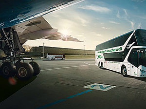 Rollfeld eines Flughafens, links der Flügel und Fahrwerk eines Fliegers, rechts ein Bus.