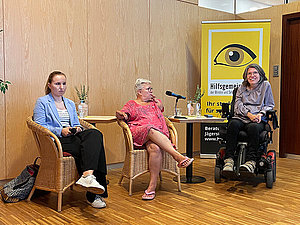 Drei Frauen unterschiedlichen Alters sitzen am Podium. Alle drei haben verschiedene Formen von Behinderungen. 