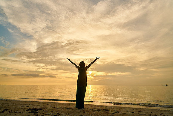 Silhouette einer Person vor Meer und Himmel, hebt Arme in die Luft.