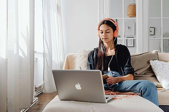 Eine junge Frau sitzt vor einem Laptop. Sie hat Kopfhörer aufgesetzt.