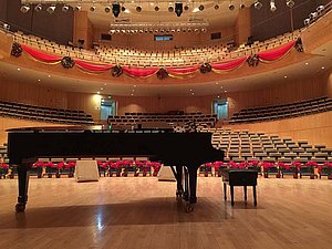 Ein Klavier mit Hocker auf einer Bühne in einer Konzerthalle