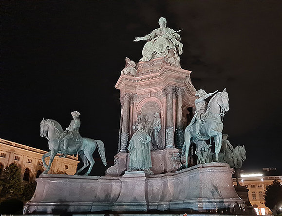 Bronzedenkmal, Kaiserin sitzt in der Mitte auf einem Thron auf hohem Sockel, vor und hinter ihr vier Reiterstatuen und andere Figuren.