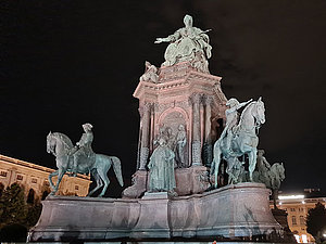 Bronzedenkmal, Kaiserin sitzt in der Mitte auf einem Thron auf hohem Sockel, vor und hinter ihr vier Reiterstatuen und andere Figuren.