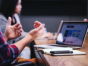 Meetingsituation: gestikulierende Hände und Laptop am Tisch mit Handy